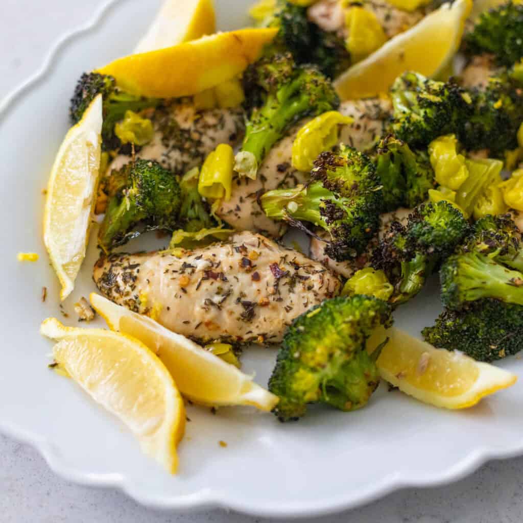 A platter of chicken and broccoli is heavily seasoned with lemon wedges on the side.
