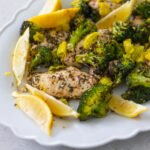 A platter of chicken and broccoli is heavily seasoned with lemon wedges on the side.