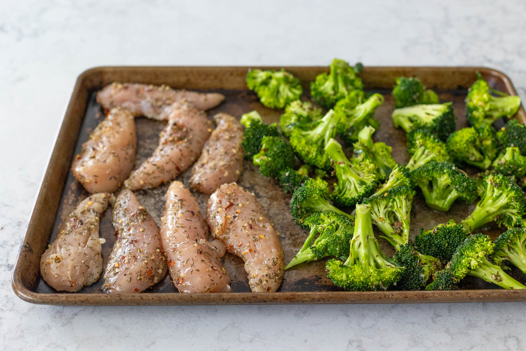 The chicken and broccoli have been seasoned and spread on a sheet pan.