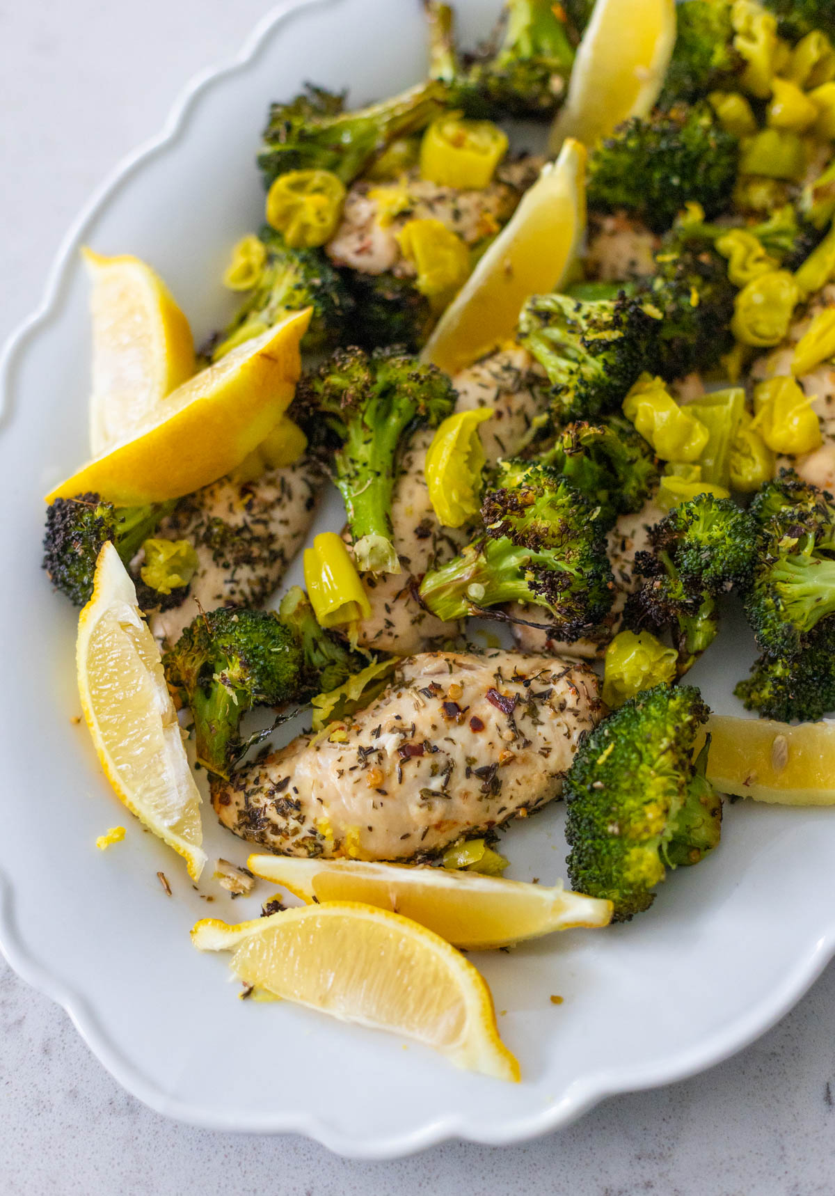The white platter is filled with chicken, broccoli, and lemon wedges.