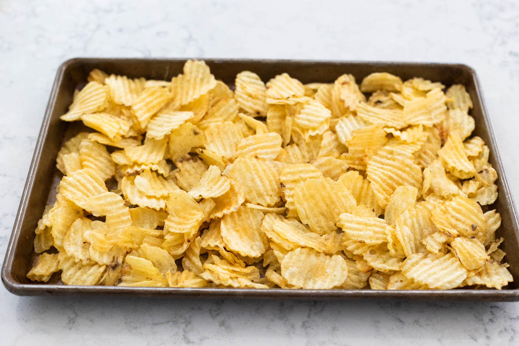 The kettle chips have been spread in an even layer on a large baking sheet.