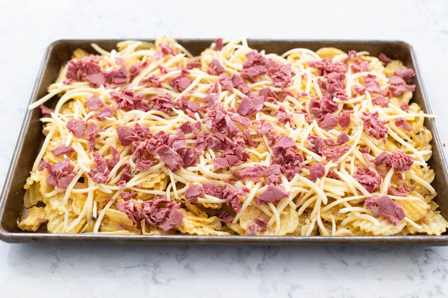 The potato chips have been covered in swiss cheese and corned beef.