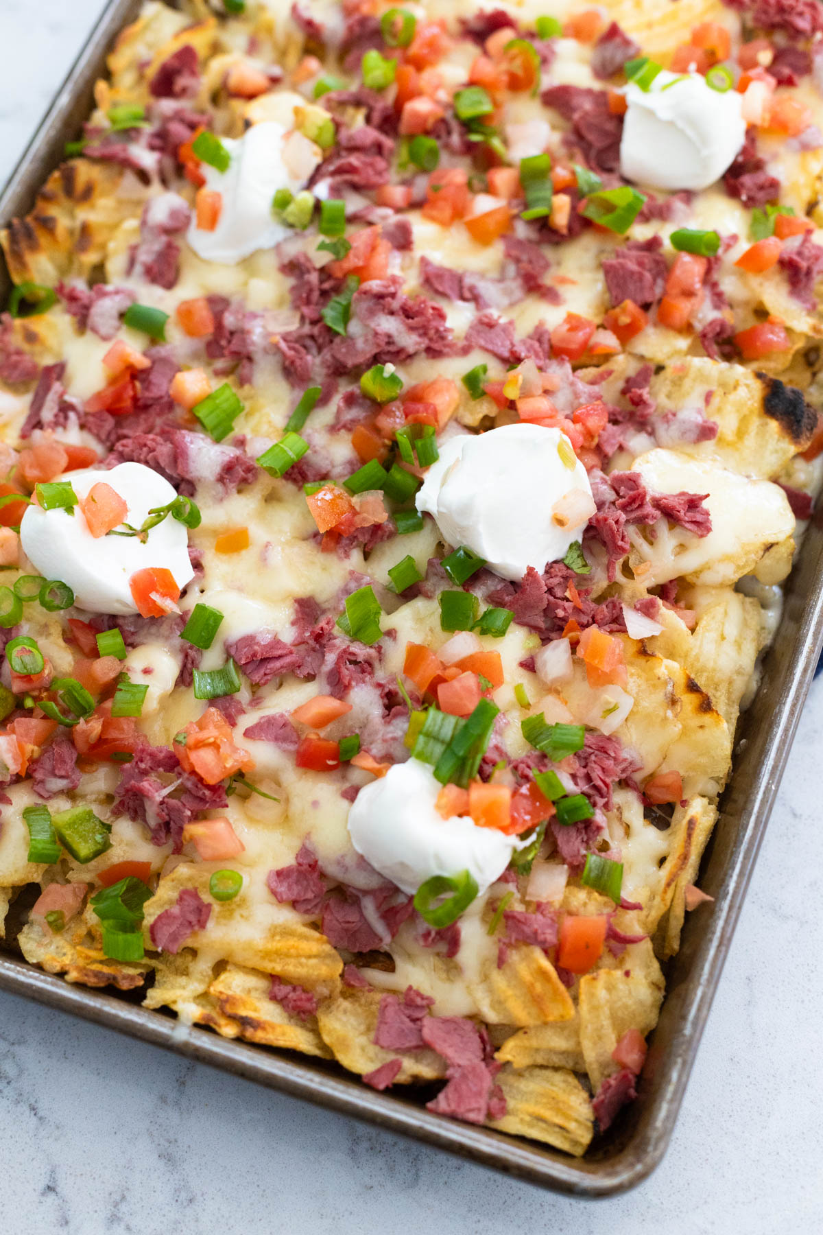 The pan of Irish nachos has been topped with sour cream, pico de gallo and green onions.
