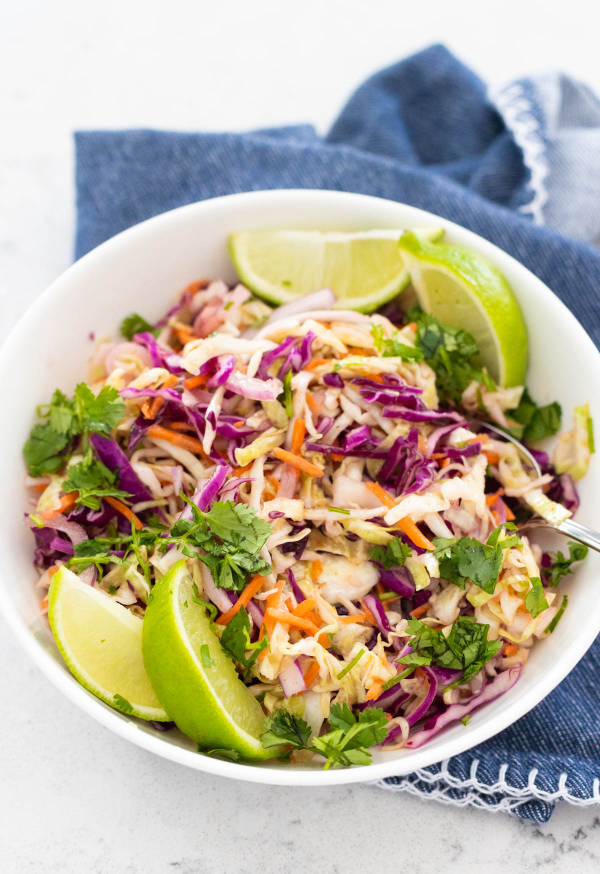 The slaw is in a white bowl with a spoon. Fresh lime wedges are on the side.