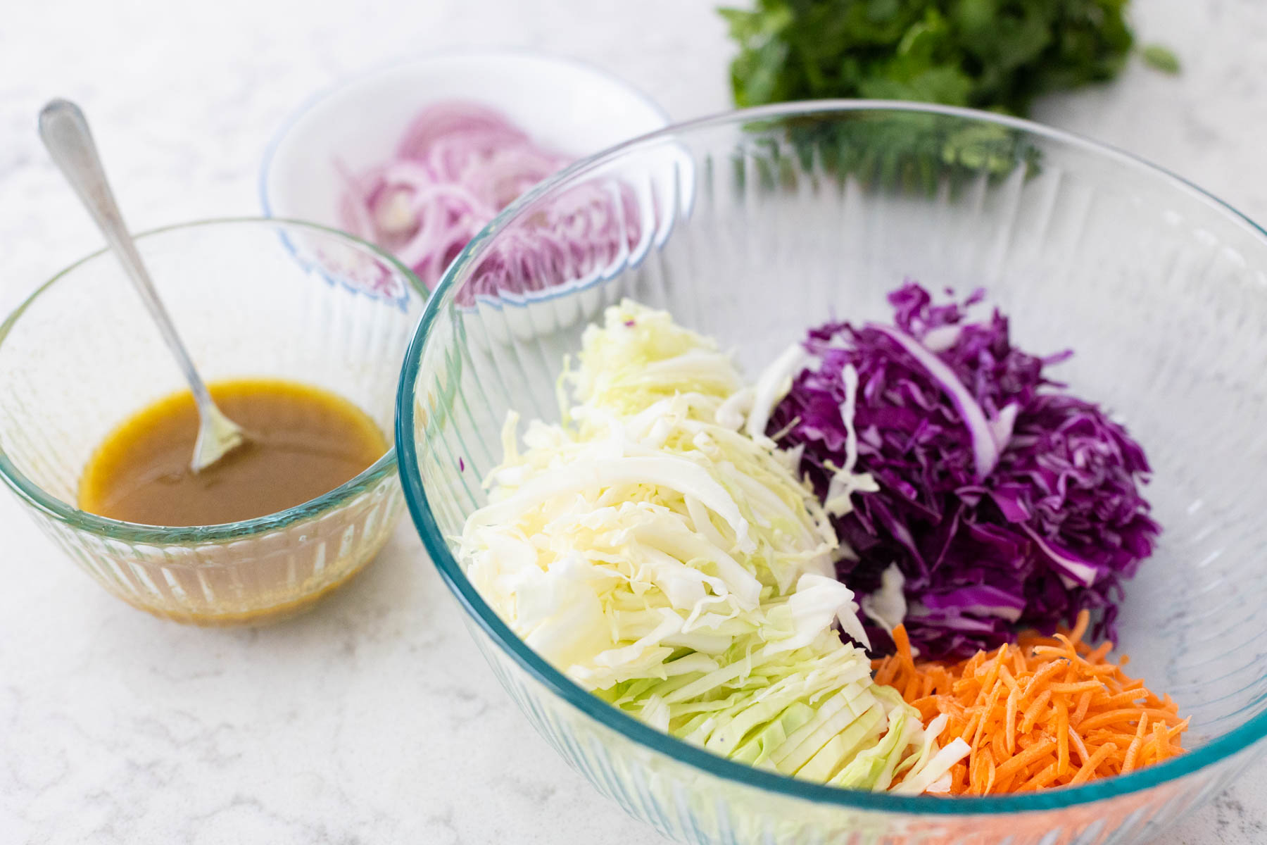 The coleslaw mix is in the bowl next to the bowl of dressing.