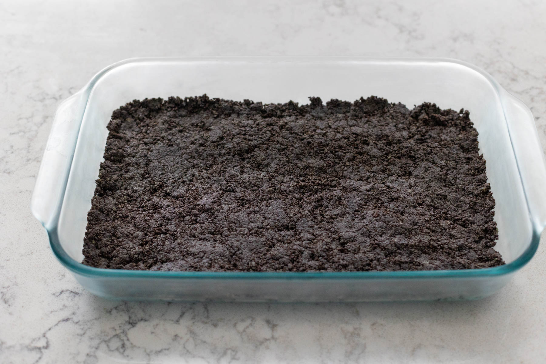 A 9x13-inch baking pan has an Oreo cookie crust waiting to be topped with a no bake dessert.
