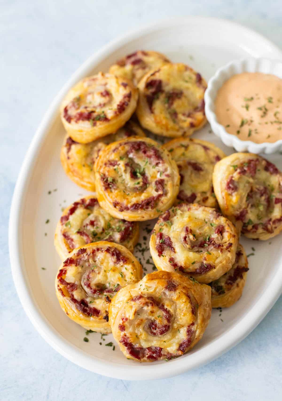 The platter is filled with the reuben pinwheels and a cup of thousand island dressing.