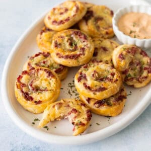 A white platter filled with reuben pinwheel bites and a cup of Thousand Island dressing.