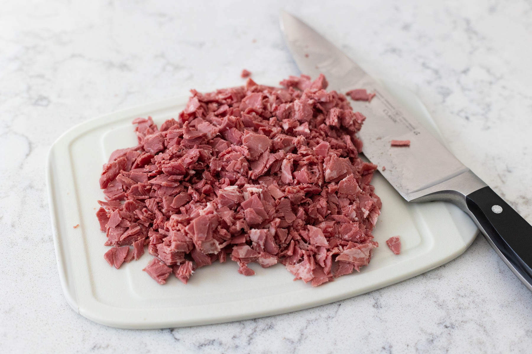 A few slices of corned beef have been chopped on a cutting board.