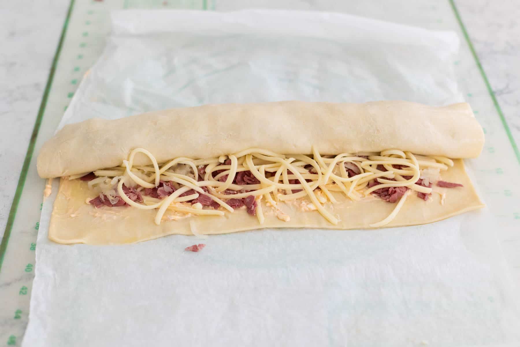 The reuben rolls are being rolled into a log towards the cook.