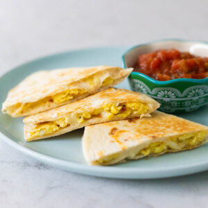 An egg and cheese breakfast quesadilla on a plate with a cup of salsa.