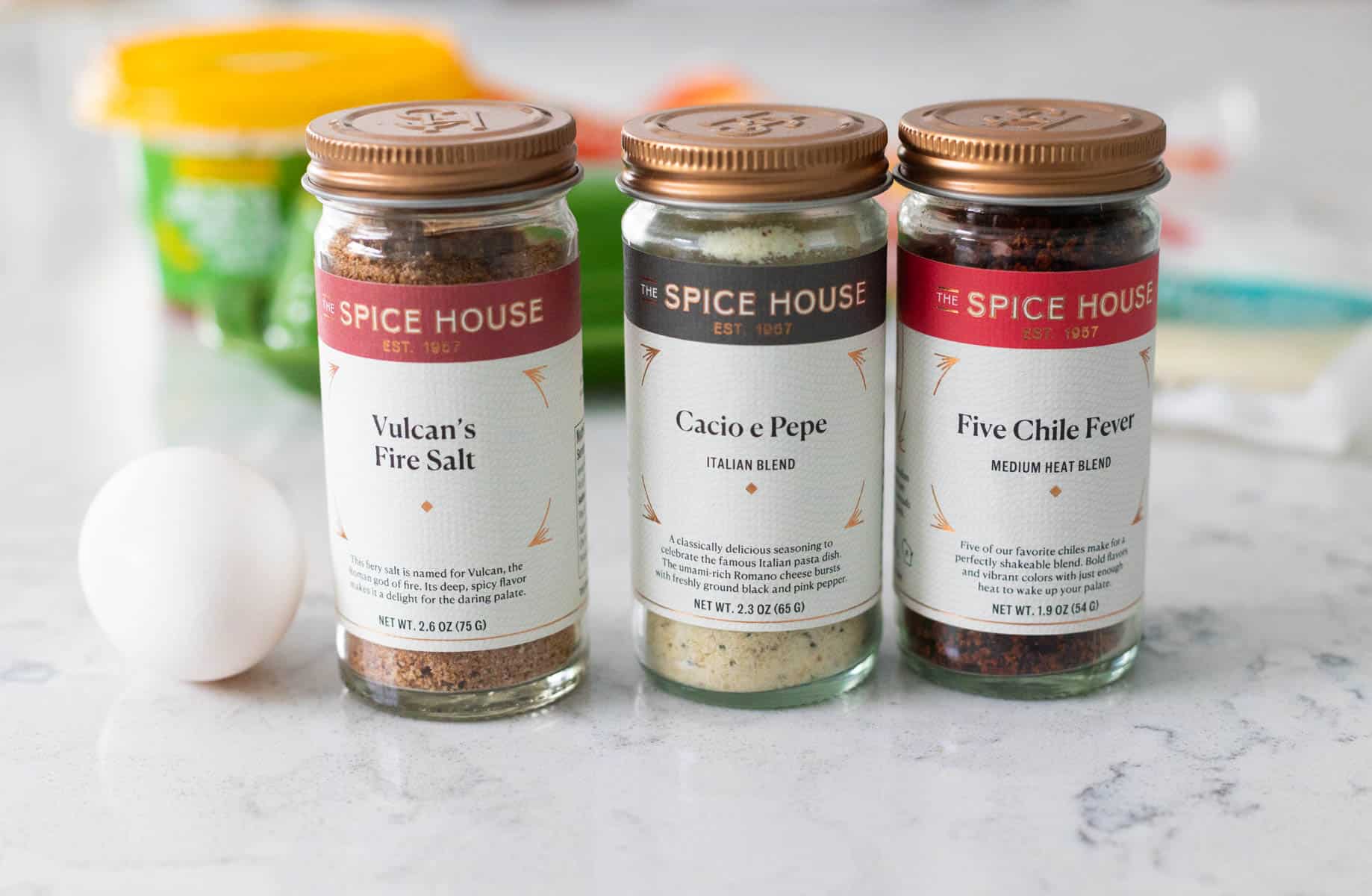3 jars of spices sit on the counter next to an egg.