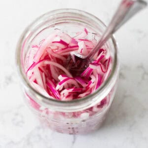 The finished red onions are in a mason jar being stirred with a fork.