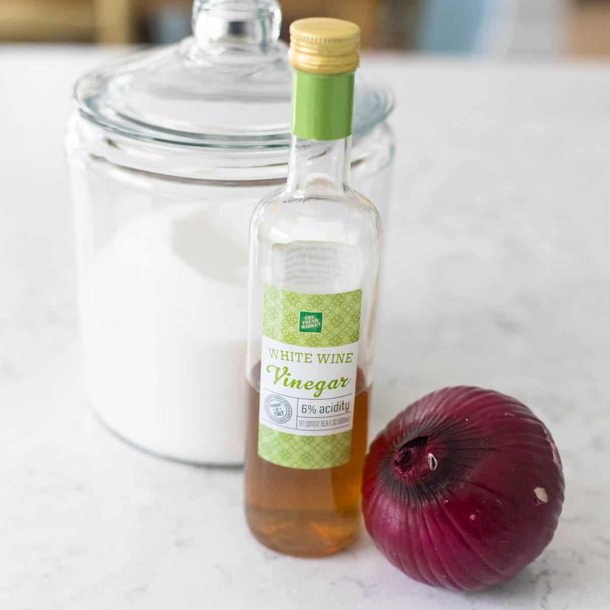 The jar of sugar, white vinegar, and onion are on the counter.