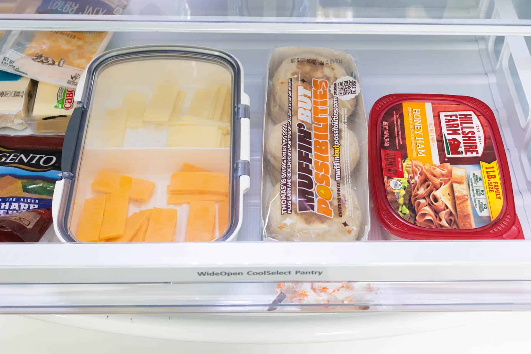 The deli drawer has sliced cheese, ham, and english muffins.