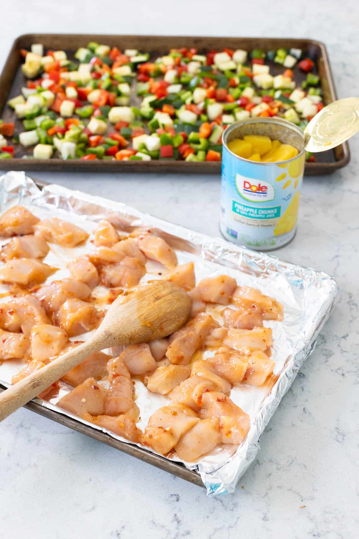 The pan of chicken and pan of vegetables are side by side with a can of pineapple is in the middle.