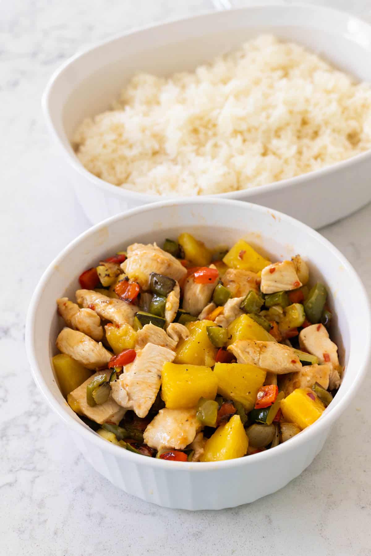 The chicken and vegetables are in a storage container next to a dish of rice.
