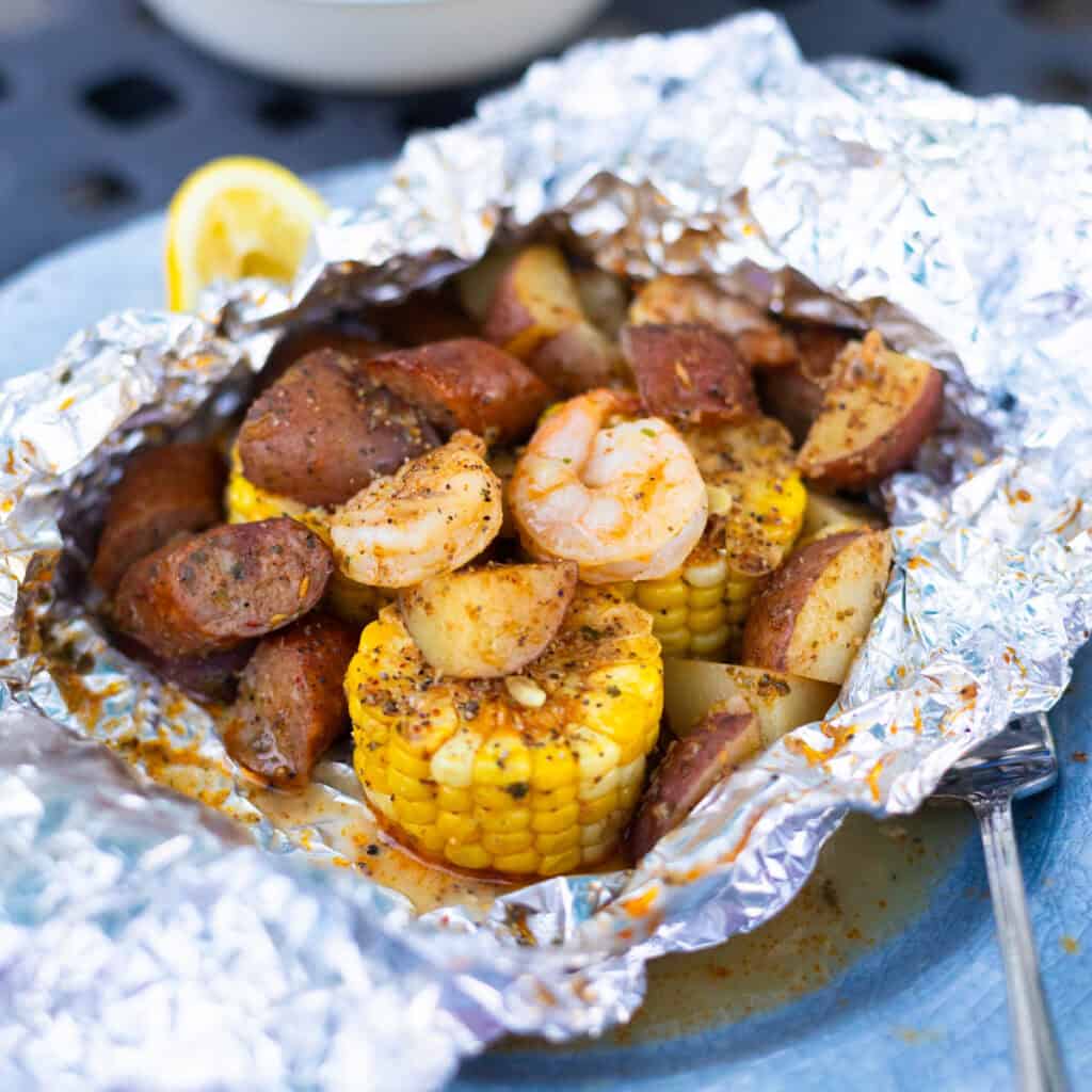 An aluminum foil packet is filled with cooked shrimp, corn on the cob, and potatoes.