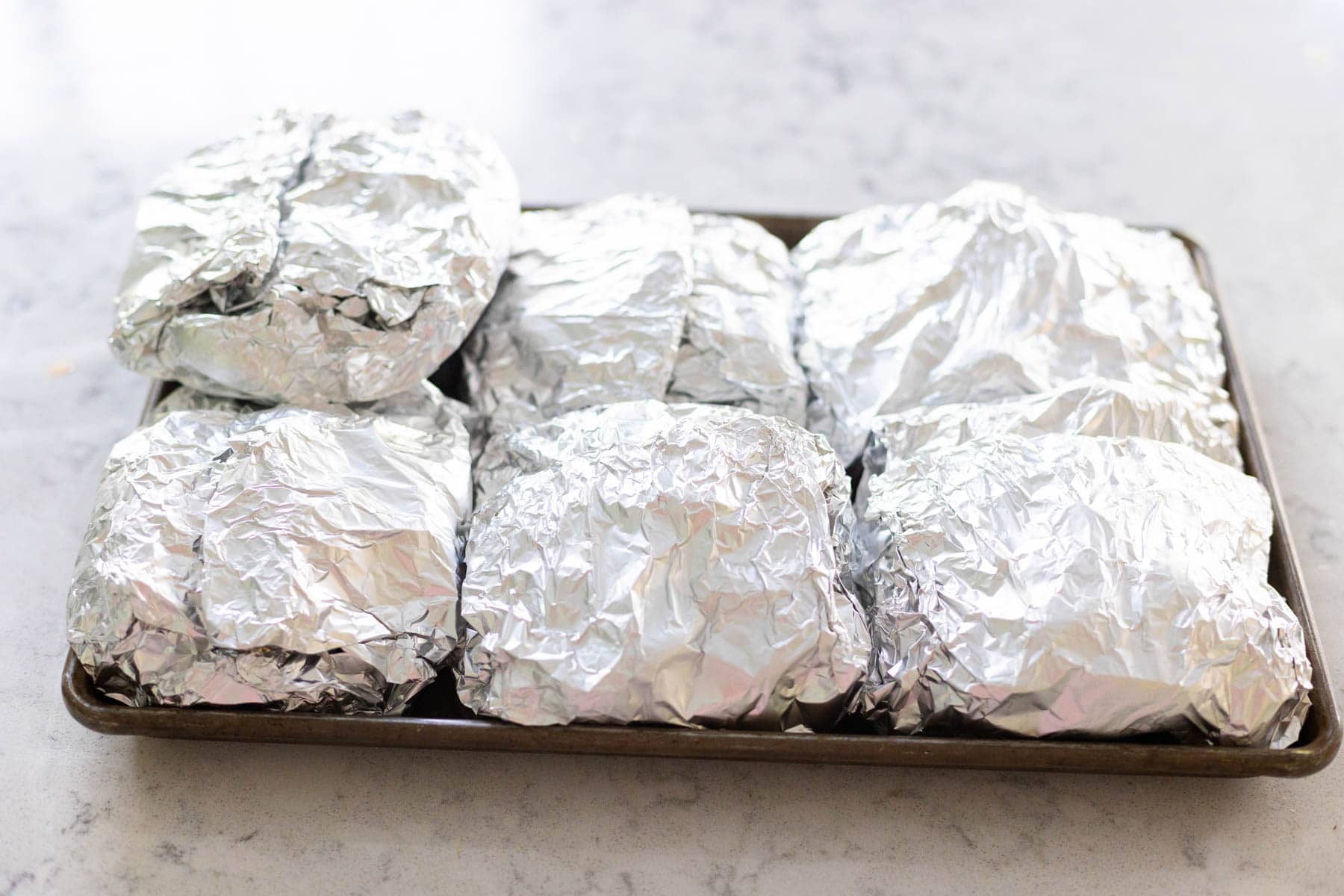 A baking sheet is filled with prepared grill packets and is about to go in the fridge.