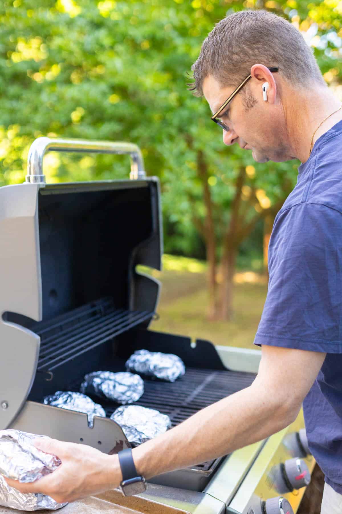 A man is placing the shrimp packets on a grill in his backyard.