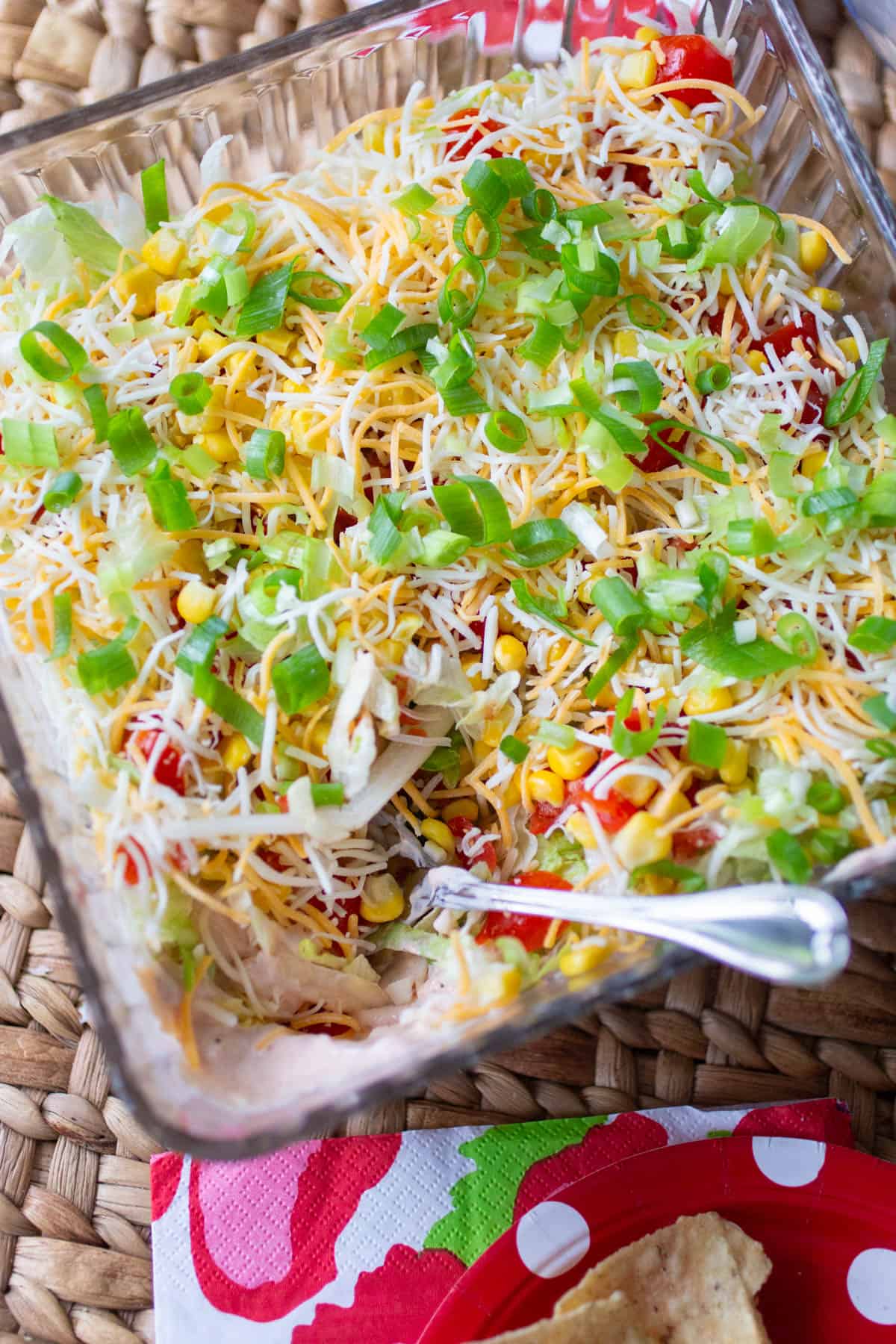 The taco dip is set out on the table at the party, a spoon is taking a scoop.