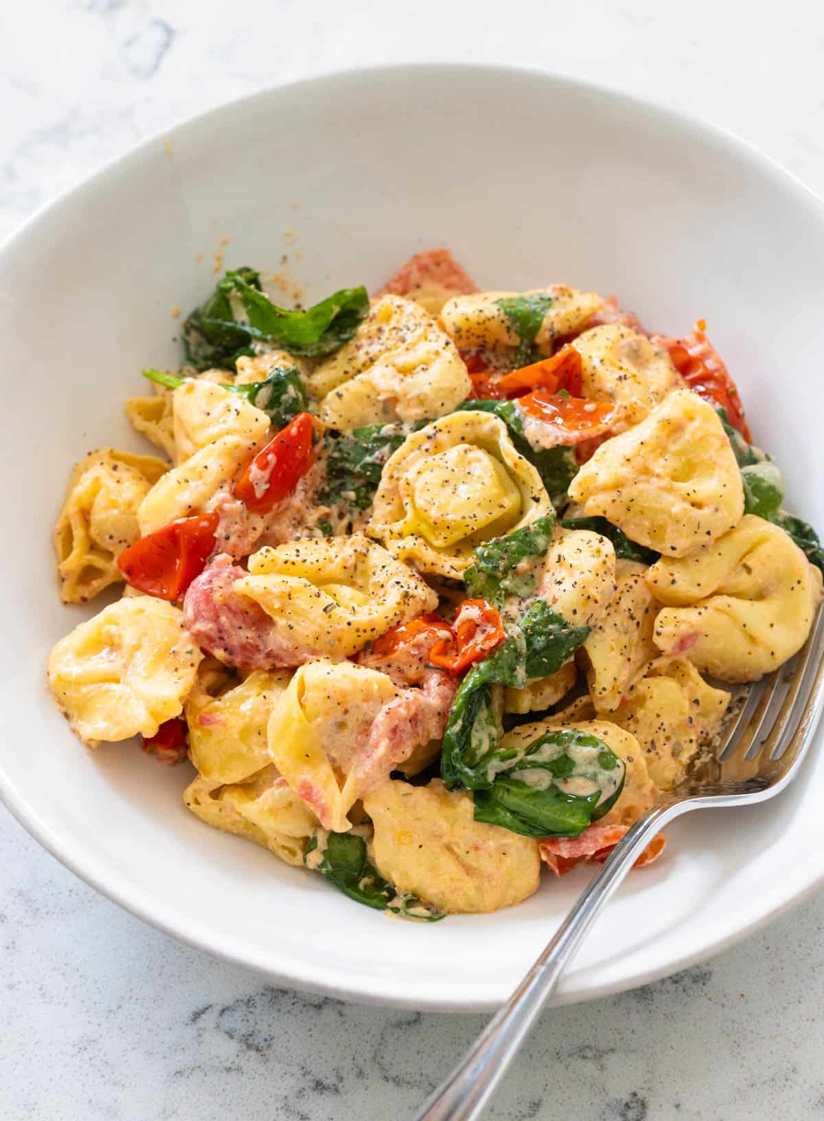 A bowl of tortellini is coated in a creamy boursin cheese sauce with tomatoes and spinach.