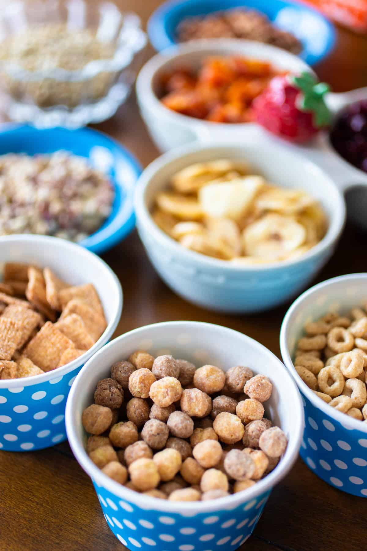 The cups of trail mix are on the table next to bowls of ingredients.