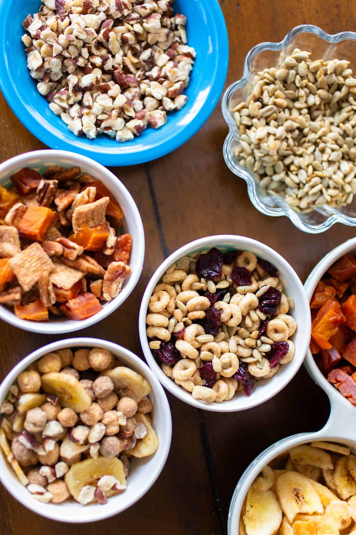 3 cups of different flavors of trail mix are on the table next to the ingredients.