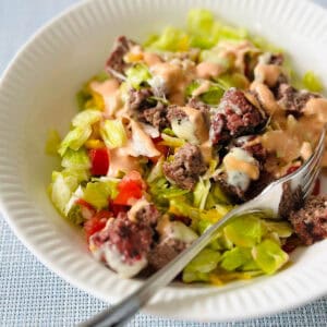 A white bowl filled with lettuce and topped with a chopped up cheeseburger.