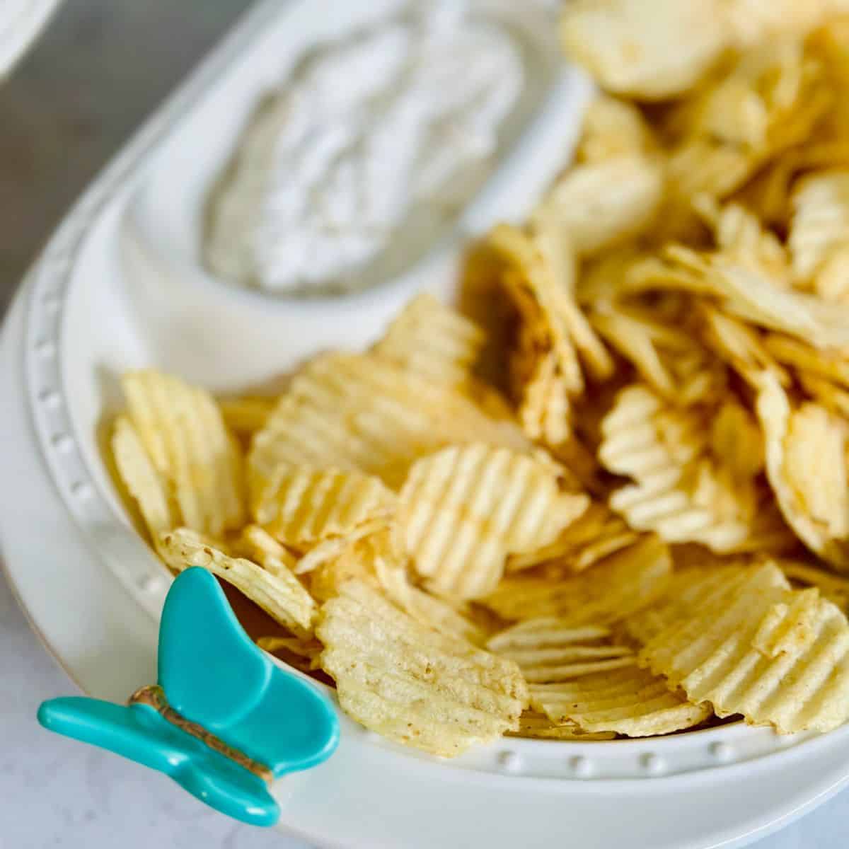 A bowl of potato chips with a creamy dip on the side.