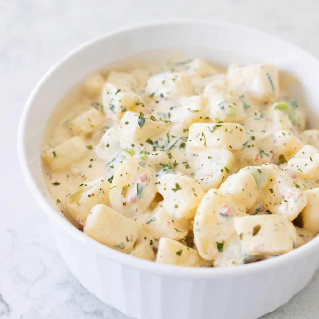 The finished ranch potato salad is in a white bowl. Parsley has ben sprinkled over the top.