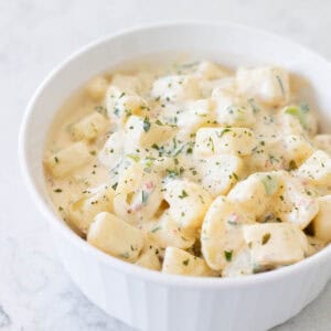 The finished ranch potato salad is in a white bowl. Parsley has ben sprinkled over the top.