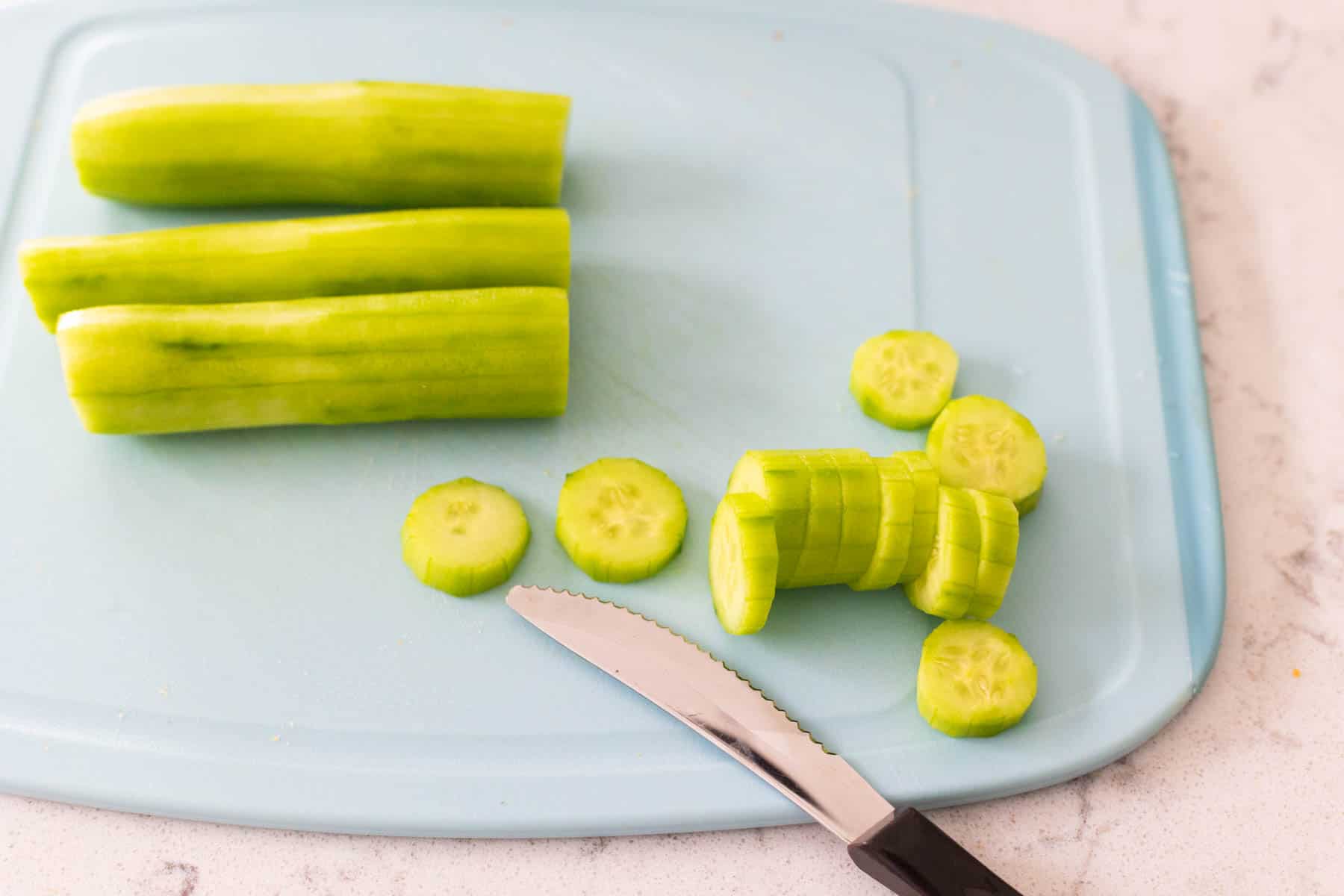 The cucumbers have been peeled and are being sliced on a cutting board with a small knife.