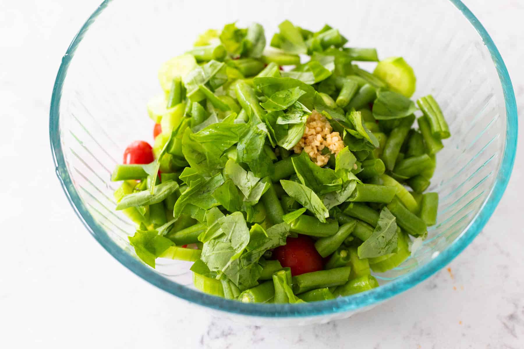 The basil has been ripped by hand and scattered over the veggies in the mixing bowl.