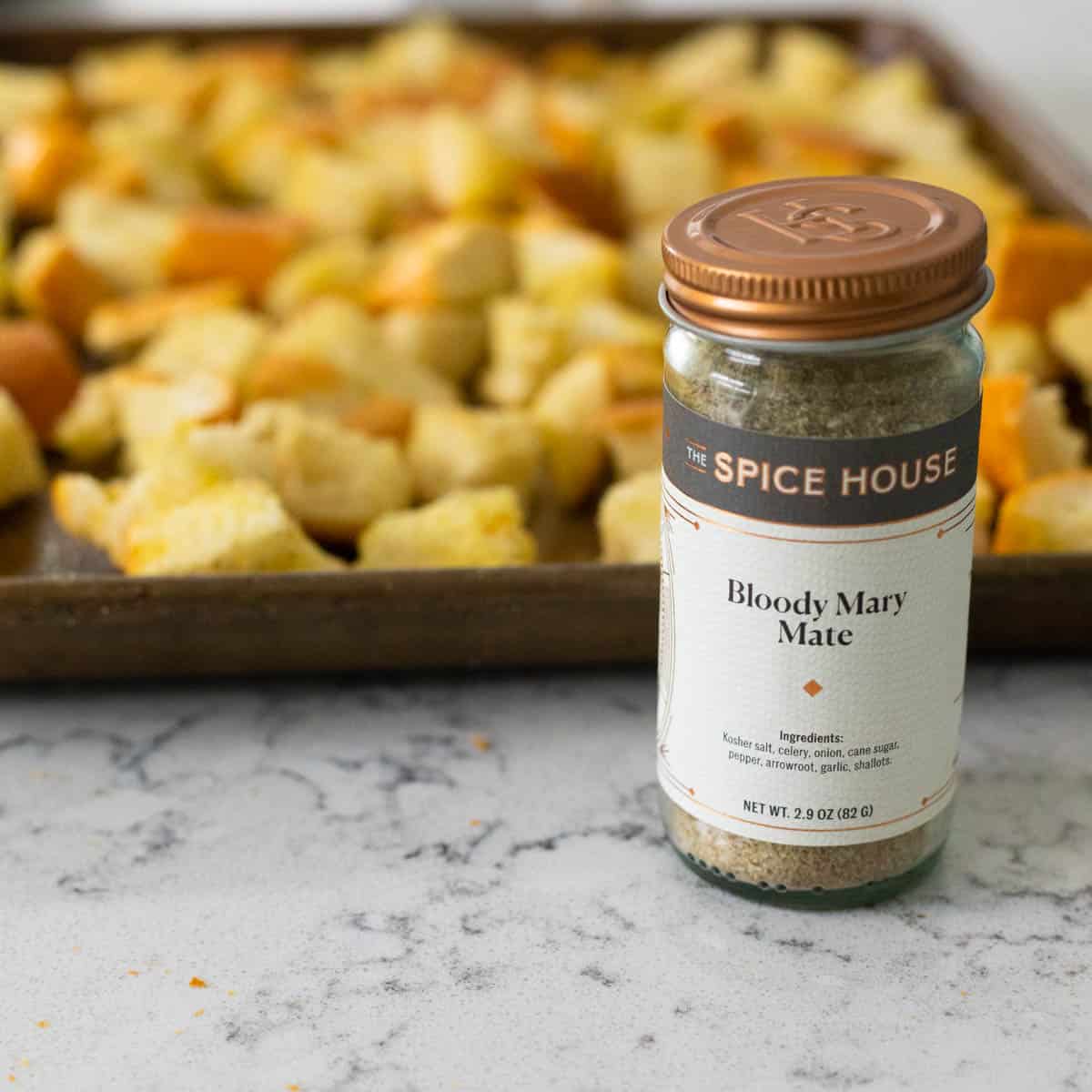 A pan of chopped baguette is on a baking sheet next to a jar of spice.