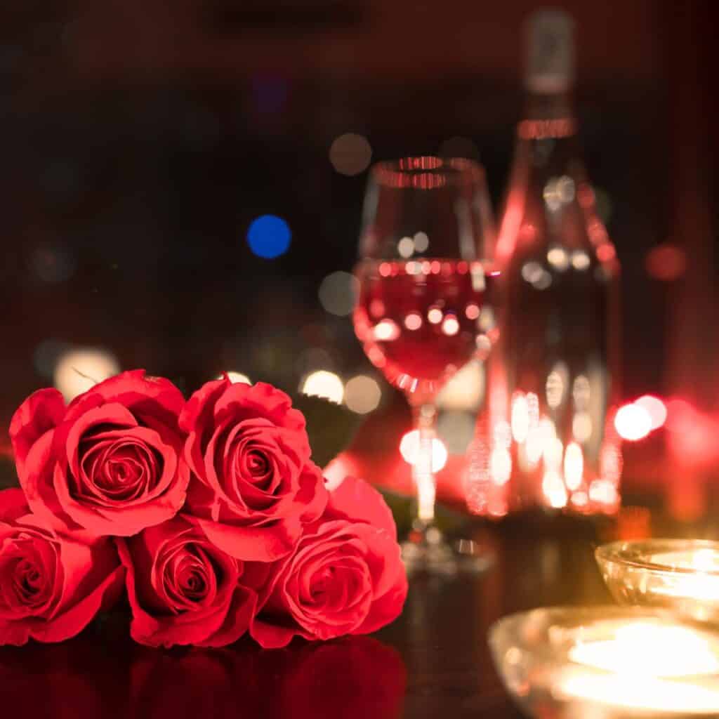 A bouquet of roses next to a glass of wine.