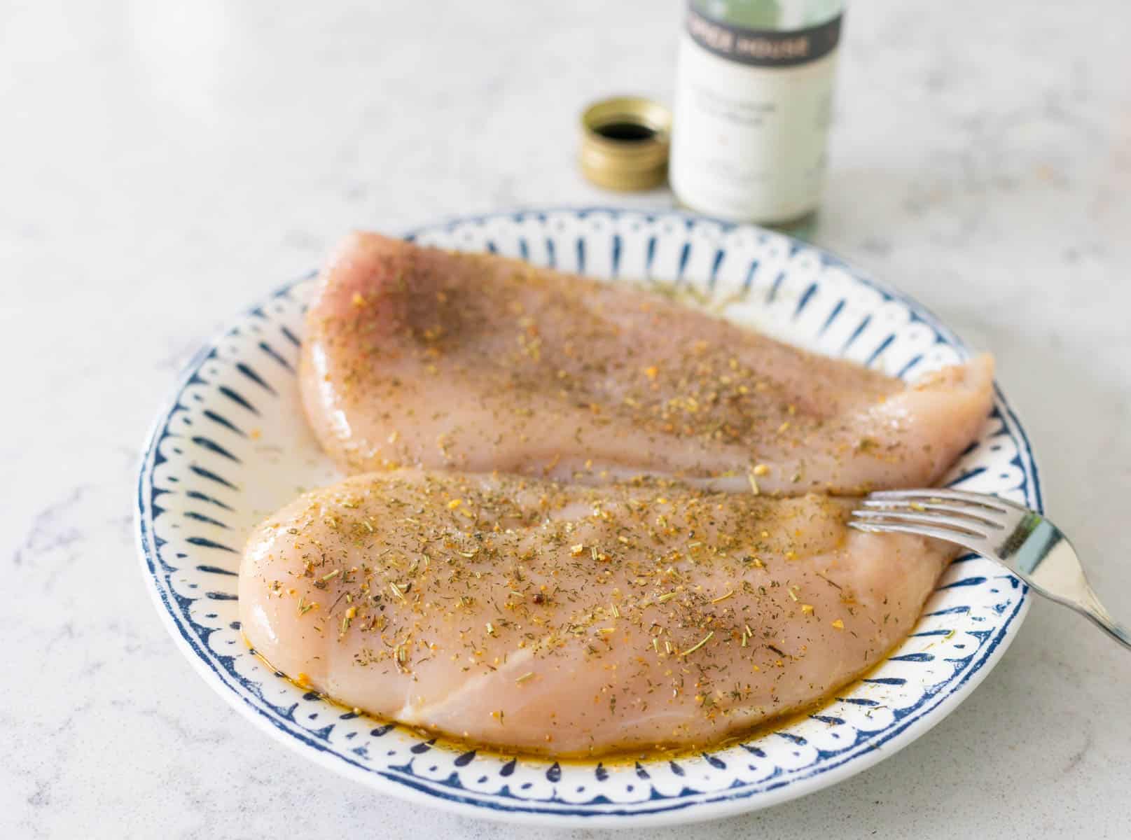 The seasoned raw chicken is on a plate next to a jar of seasoning.