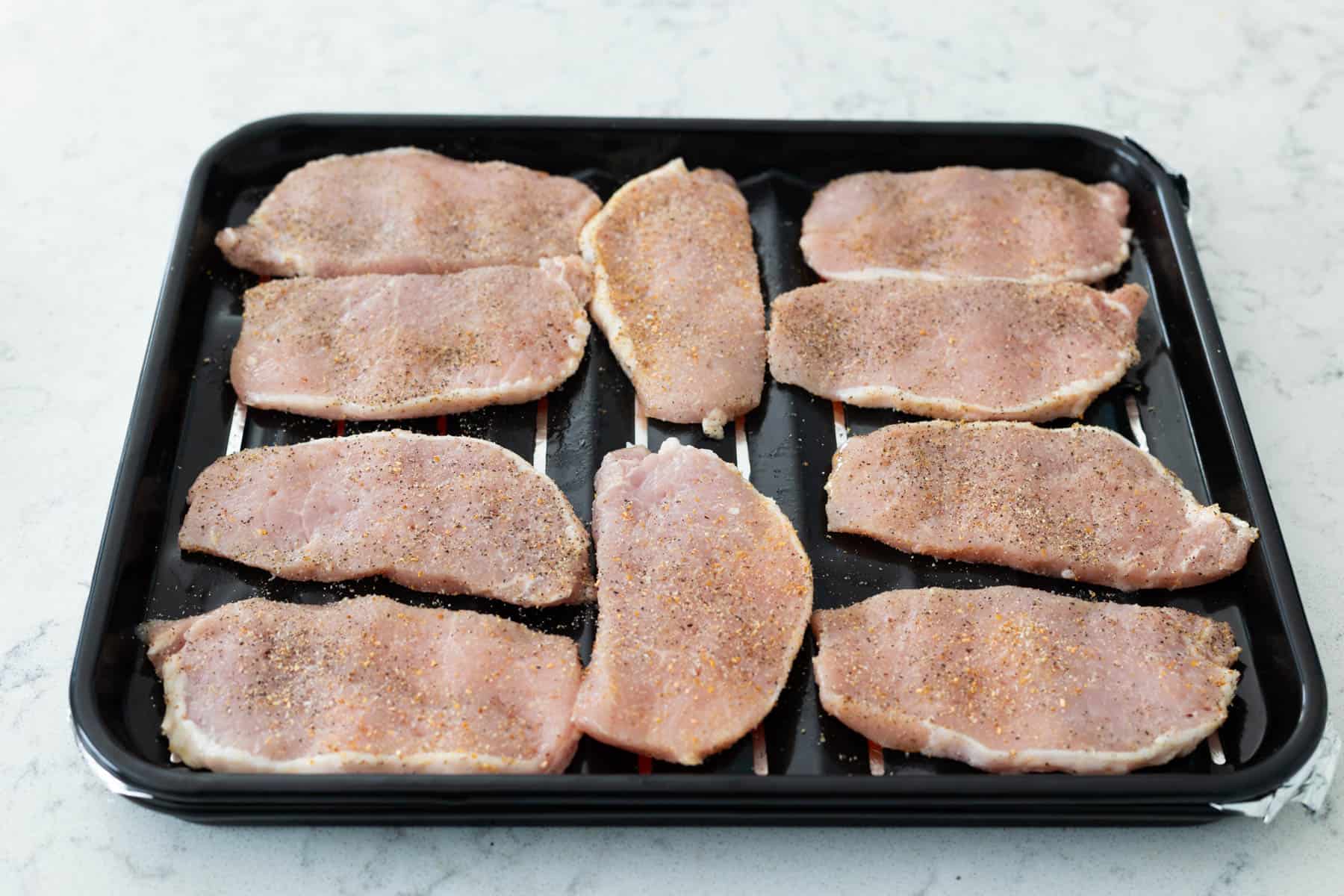 The pork chops have been arranged in a single layer on an air fryer baking pan.