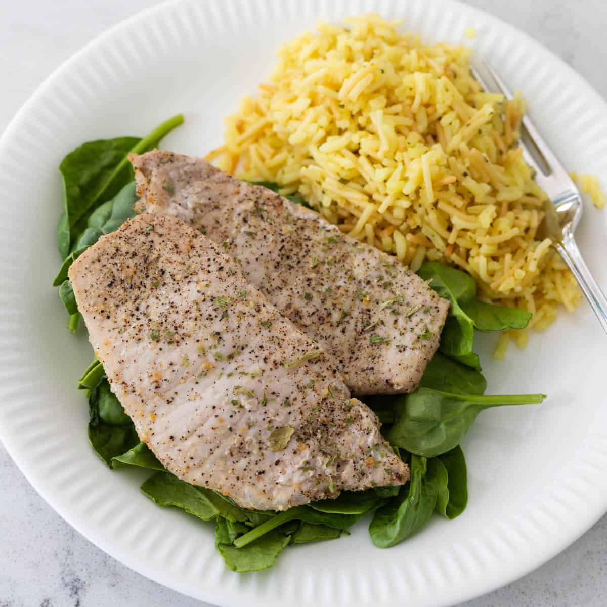 The pork chops have been served on a bed of spinach with a scoop of rice on the side.