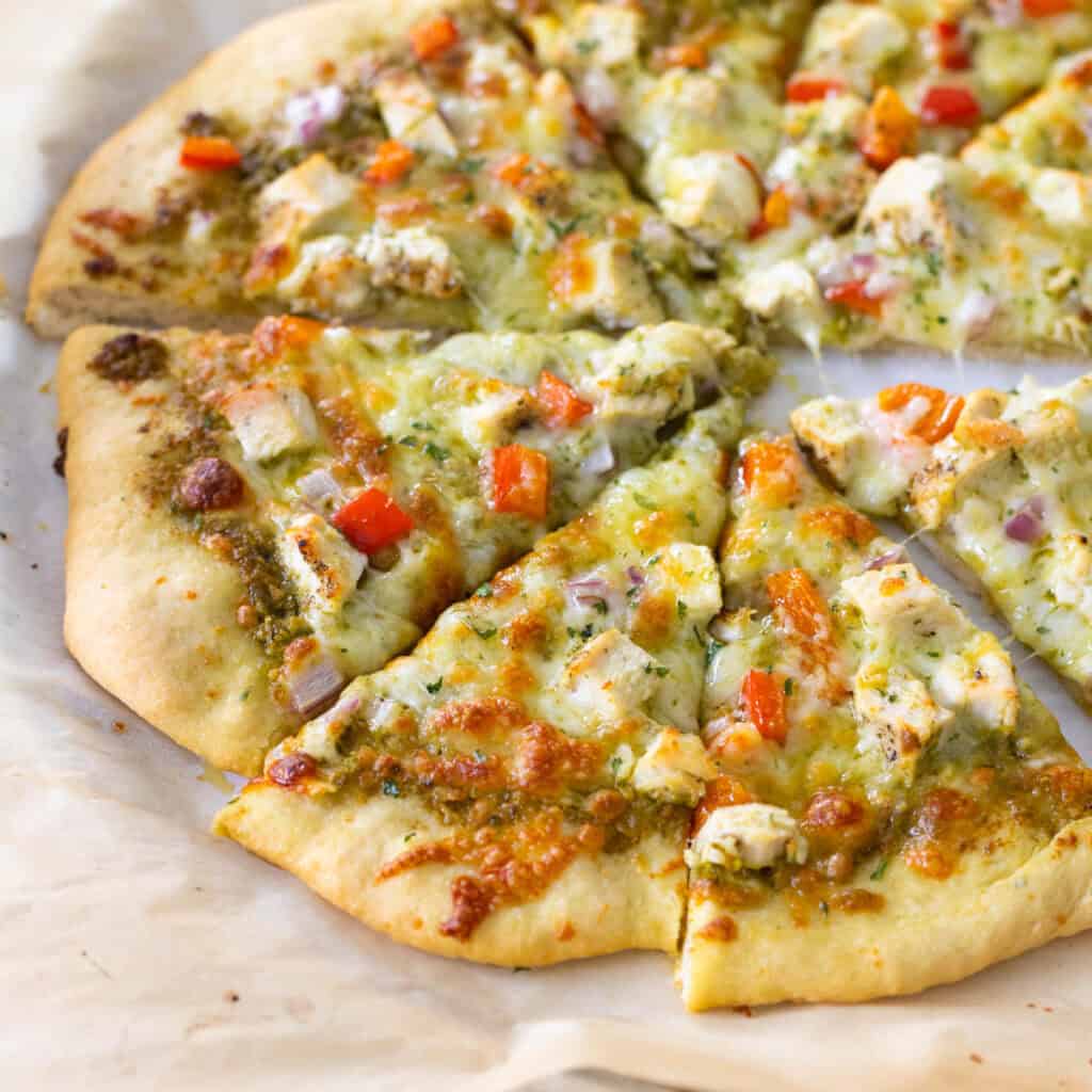 A homemade chicken pesto pizza on browned parchment paper.