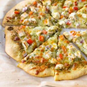 A homemade chicken pesto pizza on browned parchment paper.