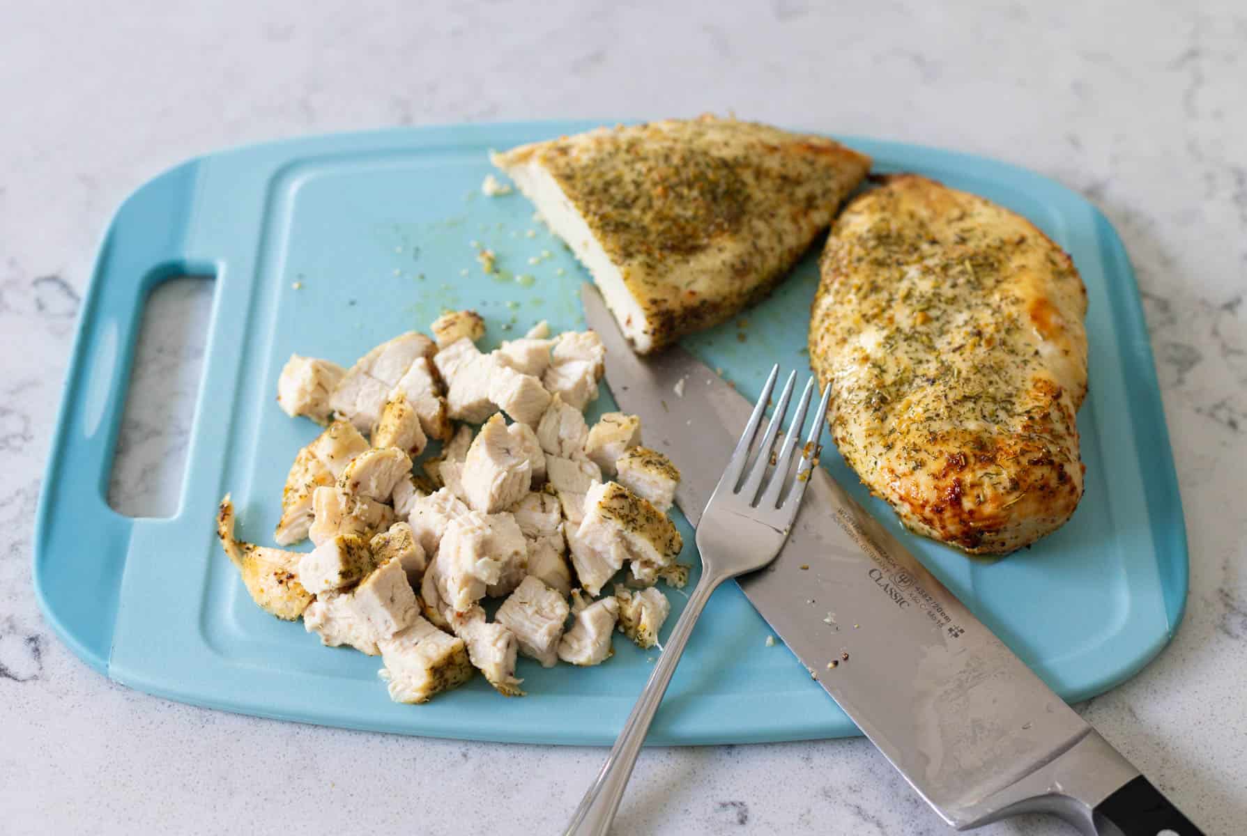 The chopped chicken breasts are on a cutting board with a chef knife.