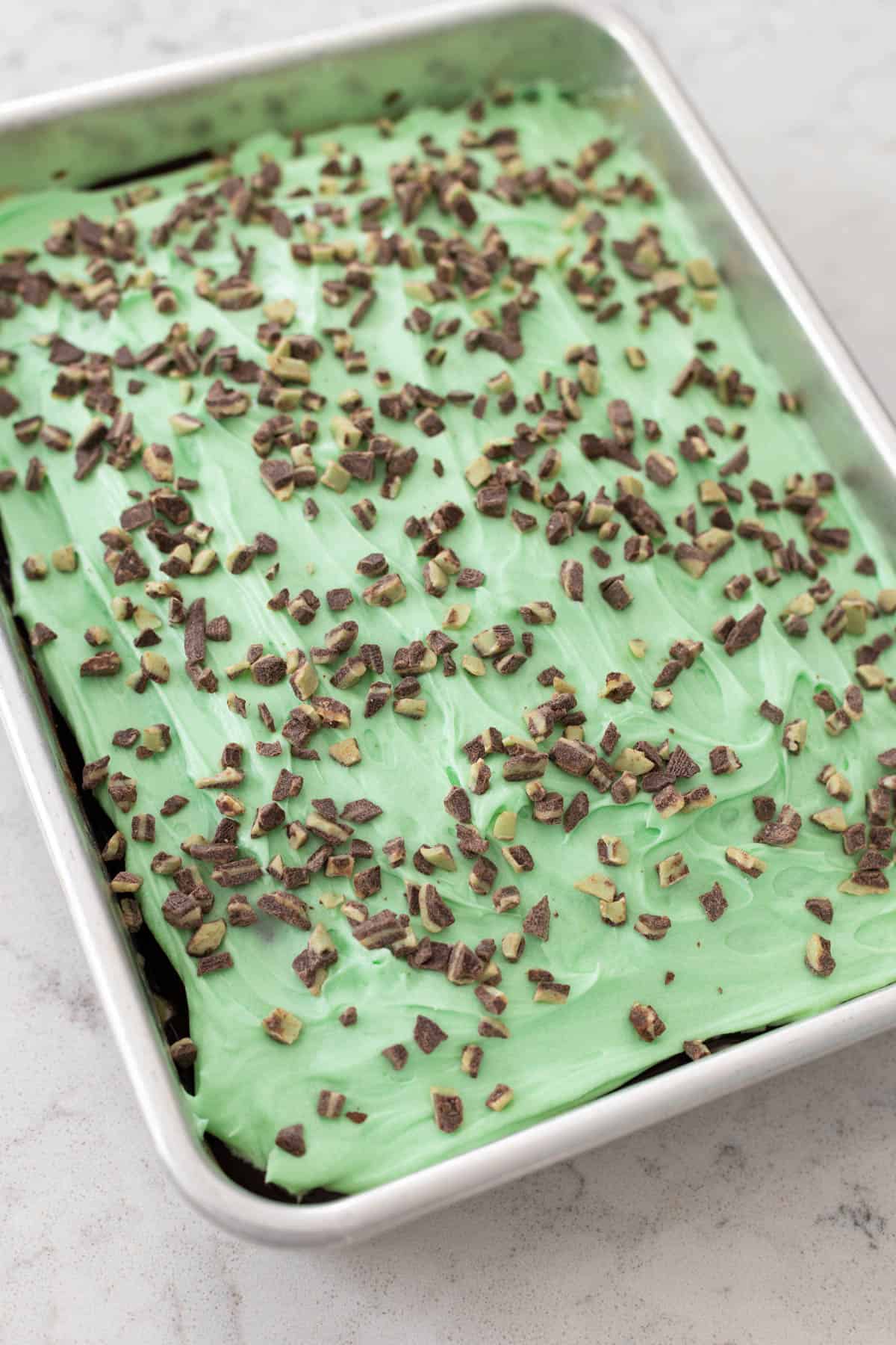 The cake has been iced with green frosting and chopped Andes candies are sprinkled over the top.