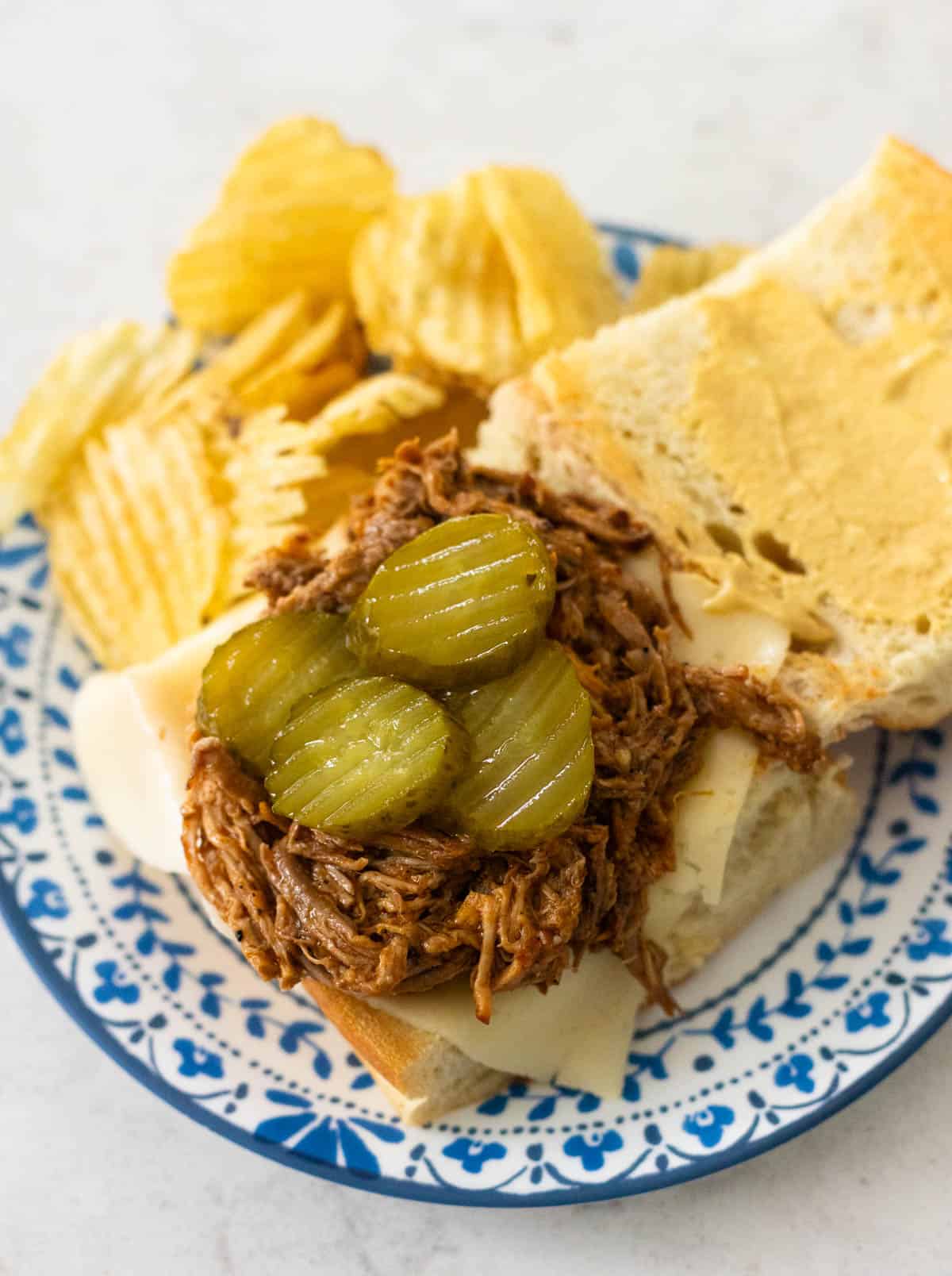 The open face Cuban pork sandwich shows the pulled pork and pickles inside.