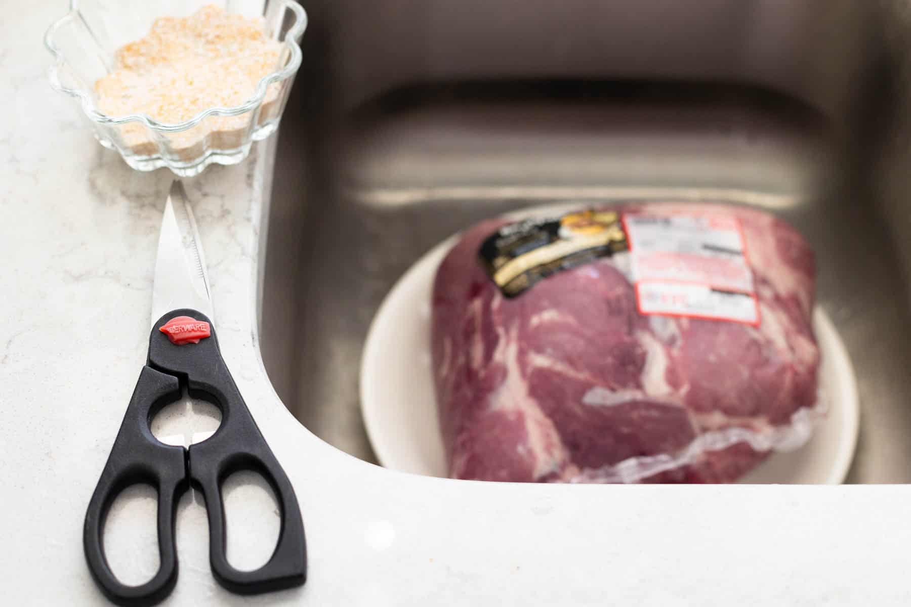 The pork shoulder is on a plate inside the kitchen sink ready to be seasoned.