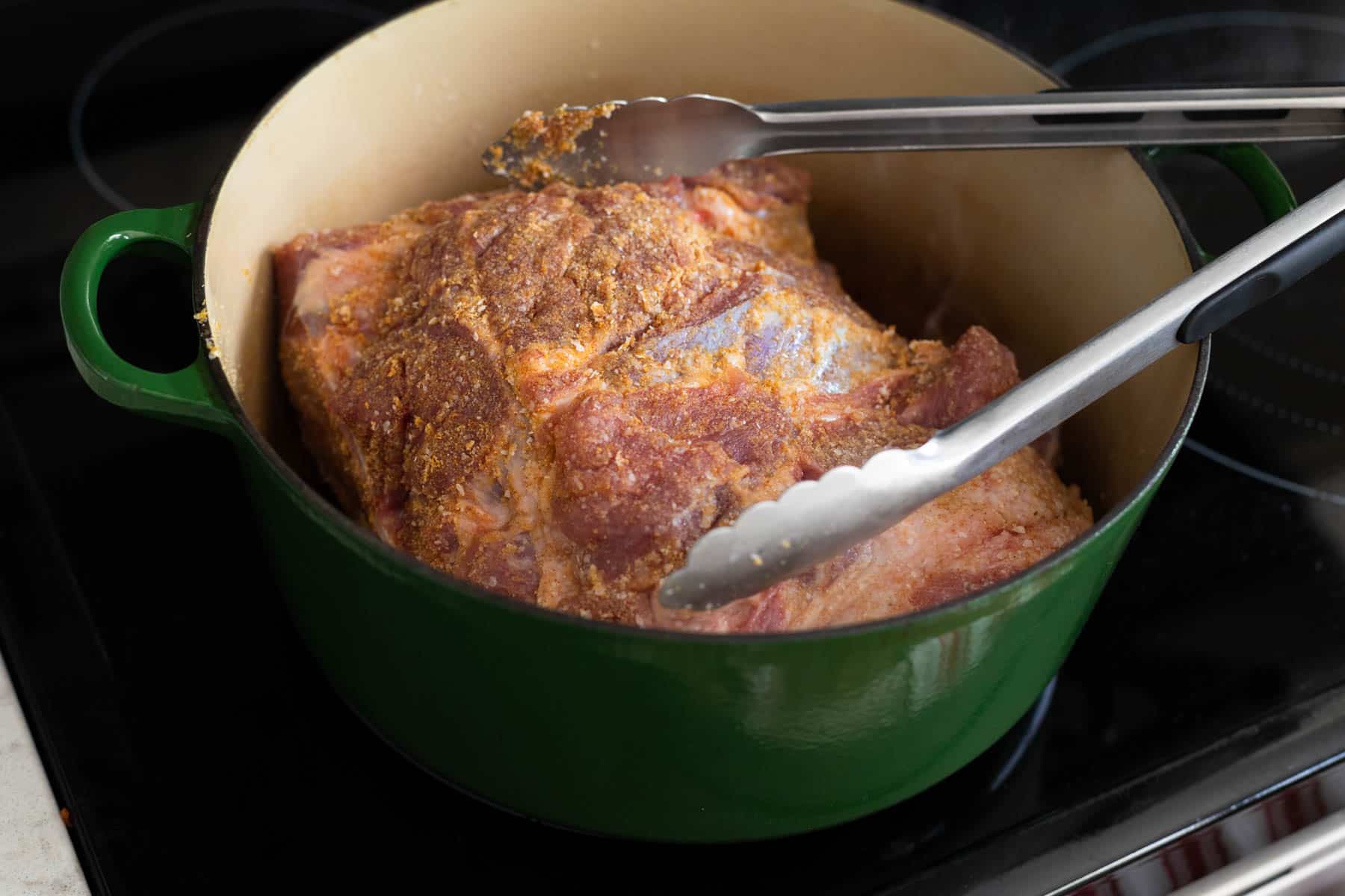 The pork is inside a dutch oven, a pair of tongs is there to flip it to brown on all sides.