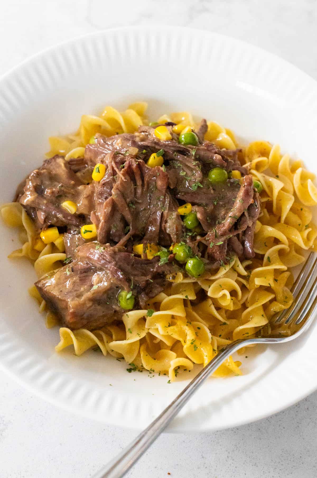 The shredded beef has been served over the wavy egg noodles.