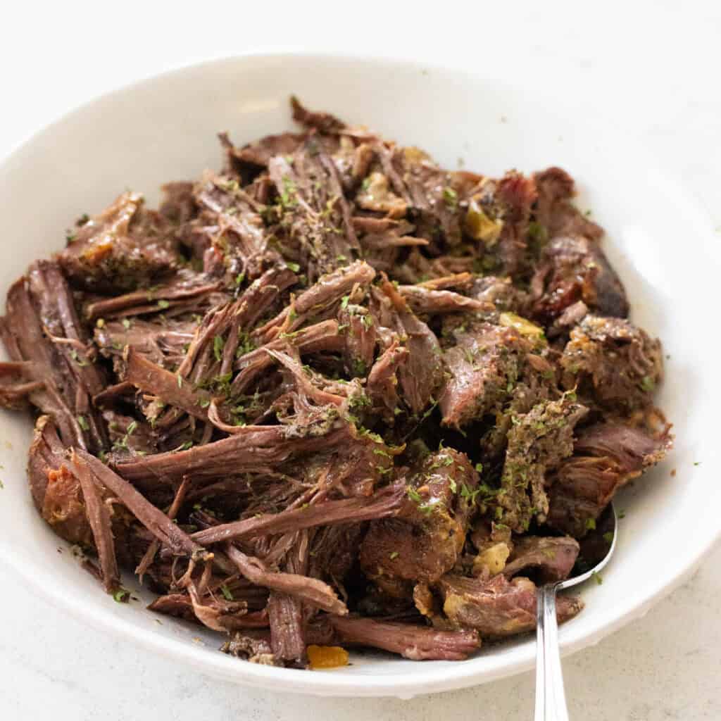 A white bowl is filled with shredded beef that was cooked in the crockpot.
