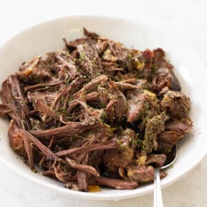 A white bowl is filled with shredded beef that was cooked in the crockpot.