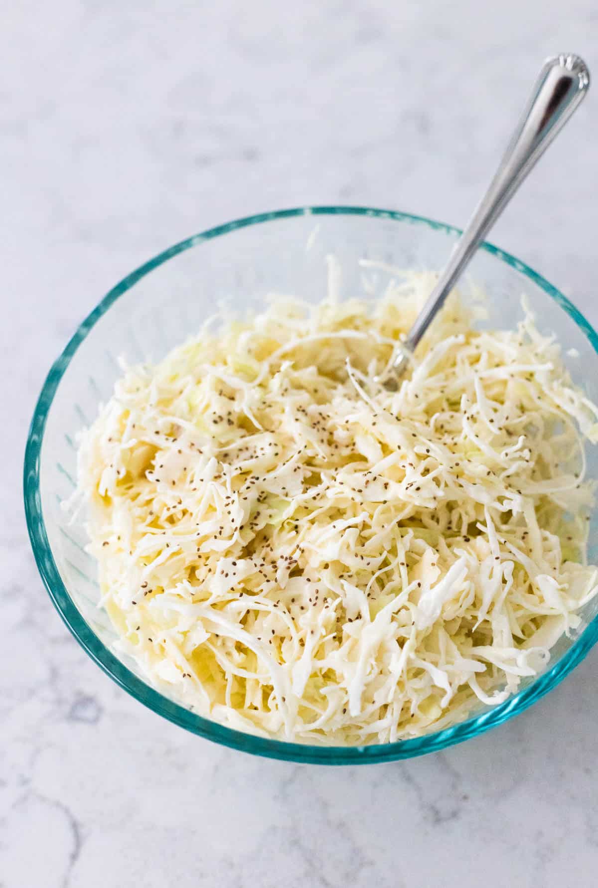 Creamy coleslaw made with angel hair sliced cabbage is in a mixing bowl.
